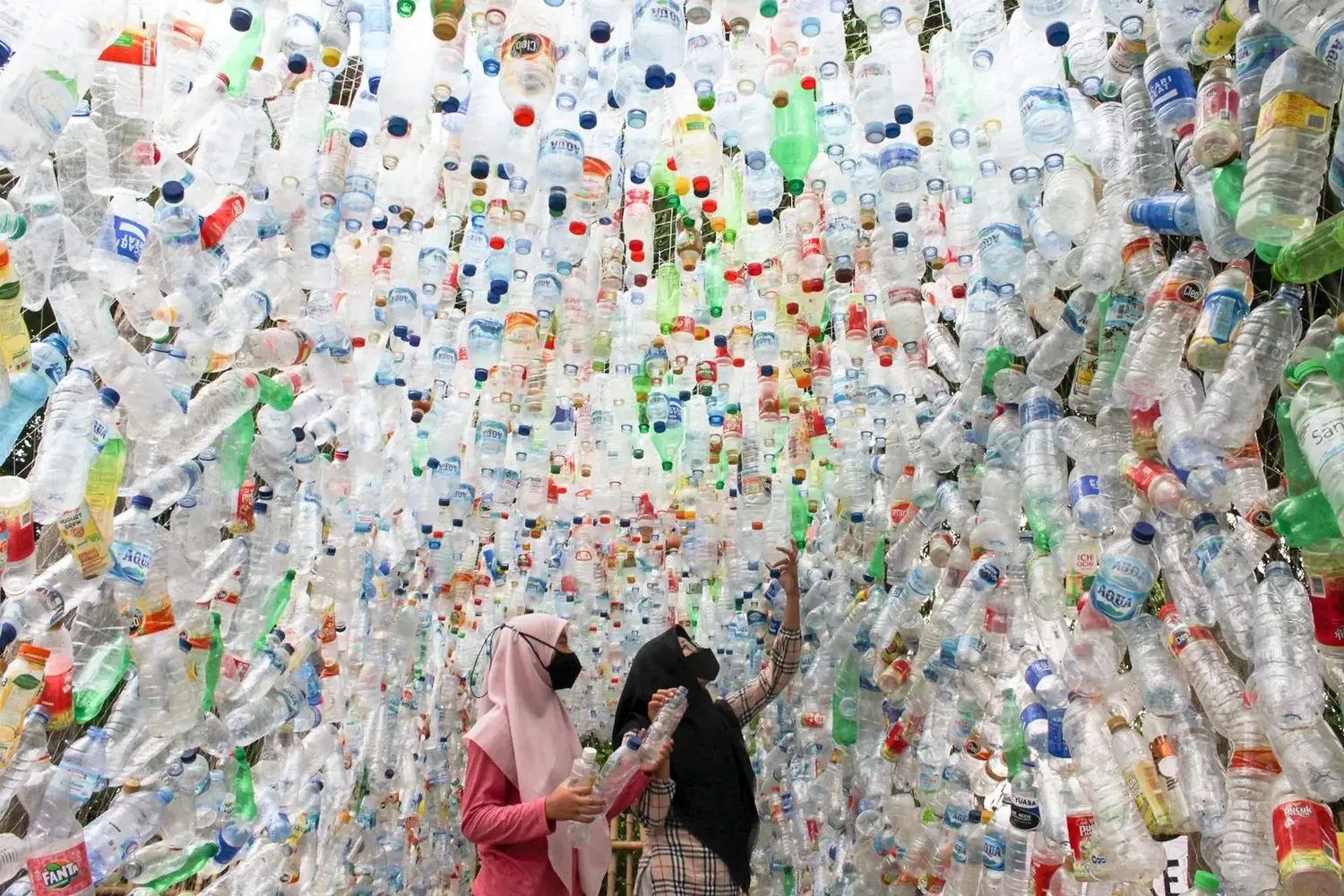 Dua perempuan memilah botol plastik di sebuah ruang komunitas.