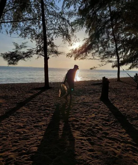 Siluet seorang pemulung di tepi pantai saat matahari terbenam.