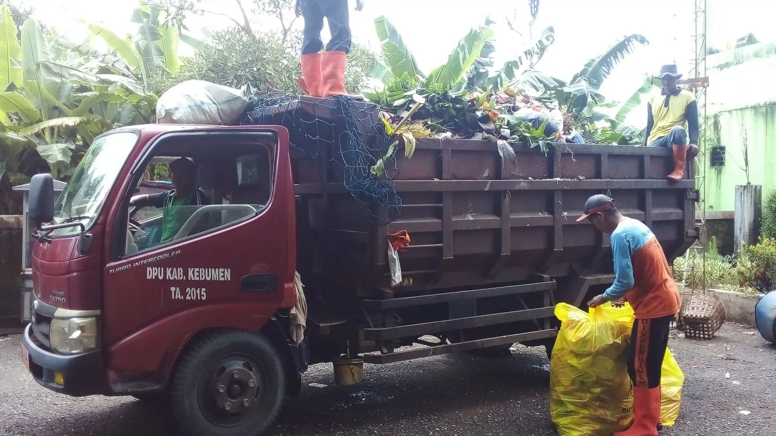 Truk pengangkut sampah dan dua petugas di area pengelolaan sampah.